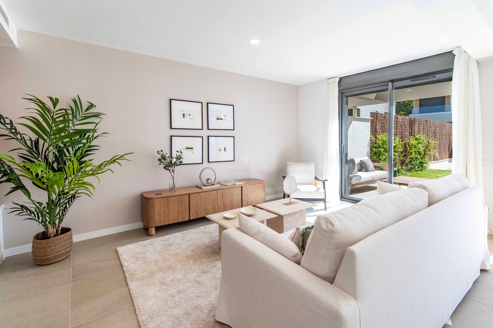 Helles Wohnzimmer mit cremefarbenem Sofa, Holz-Sideboard und Glasschiebetüren zu einer sonnigen Gartenterrasse.