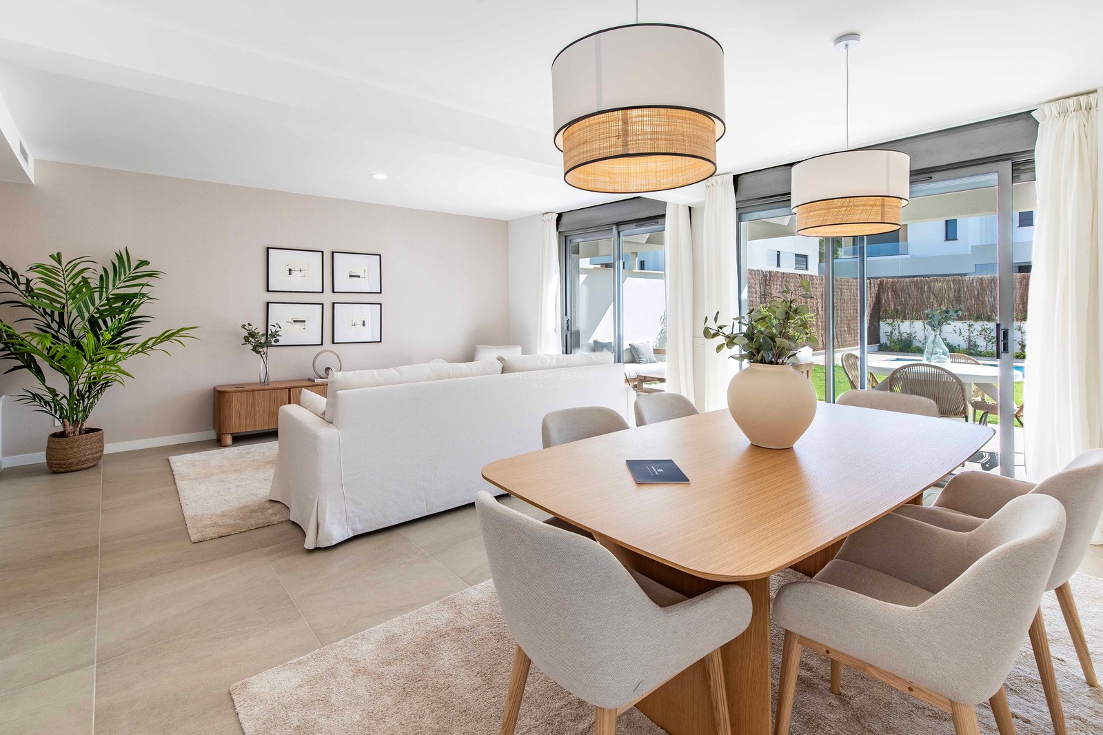 Modernes Wohnzimmer mit Eichentisch, hellem Sofa und raumhohen Glasfronten zum Garten und Pool.