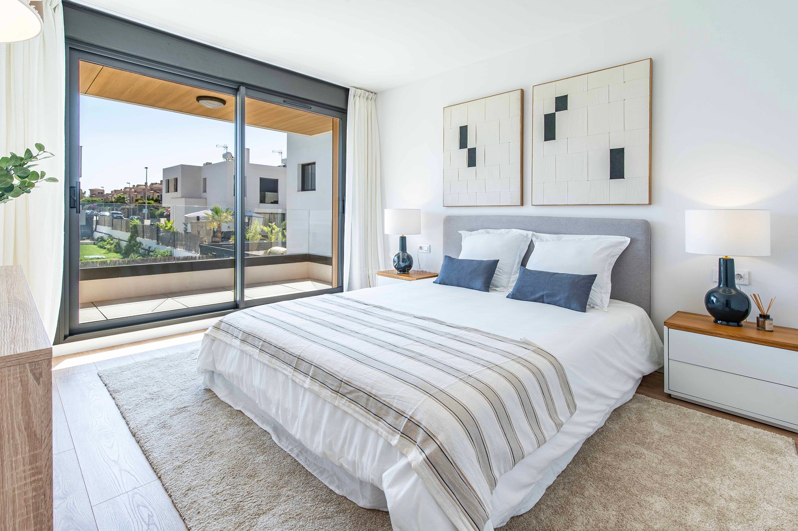 Helles, modernes Hauptschlafzimmer mit großem Doppelbett, neutralen Tönen und Glasschiebetüren zur Terrasse.