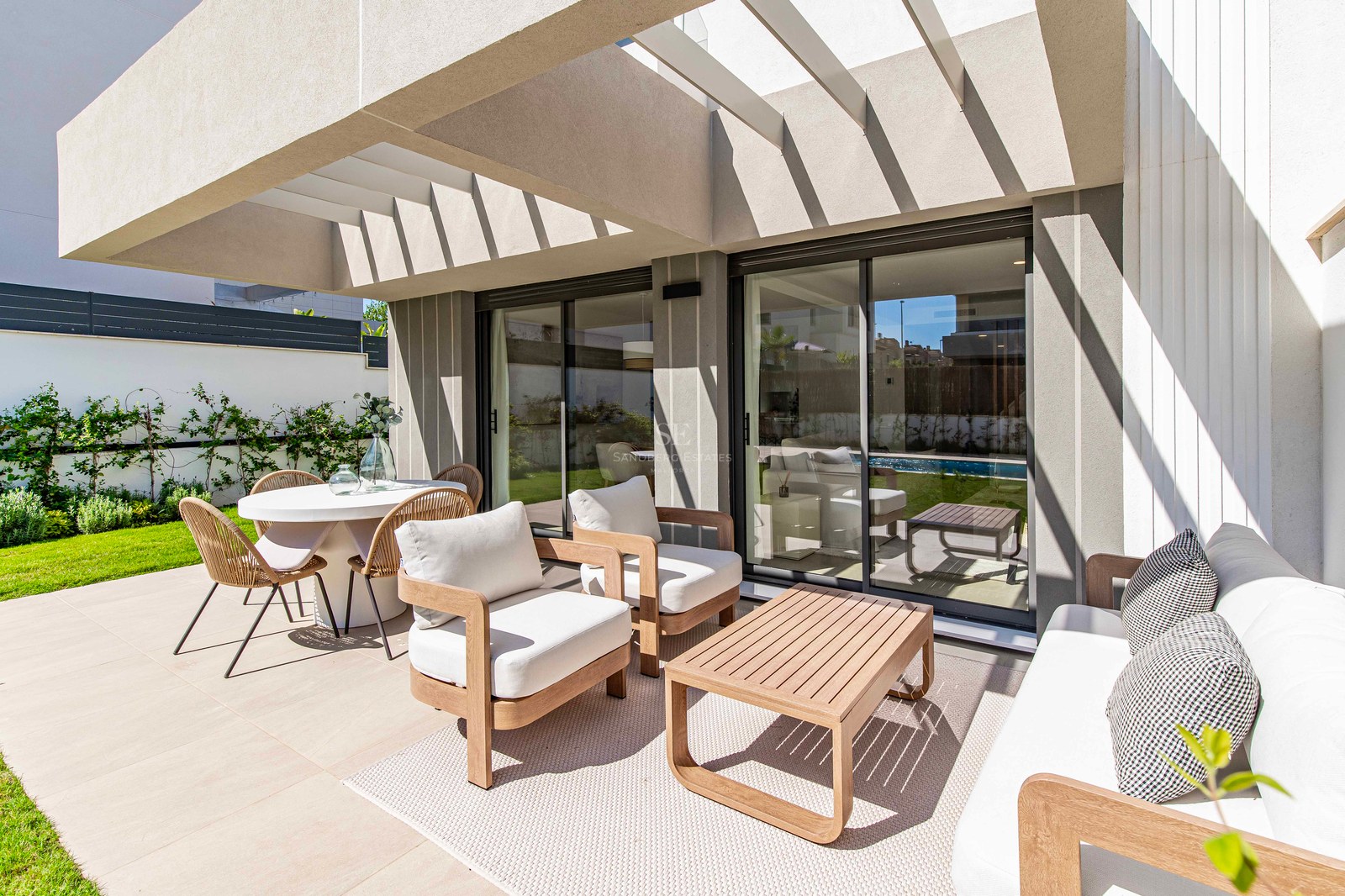 Terrasse mit Holzmöbeln und Essbereich neben einem privaten Garten unter einer modernen Pergola.