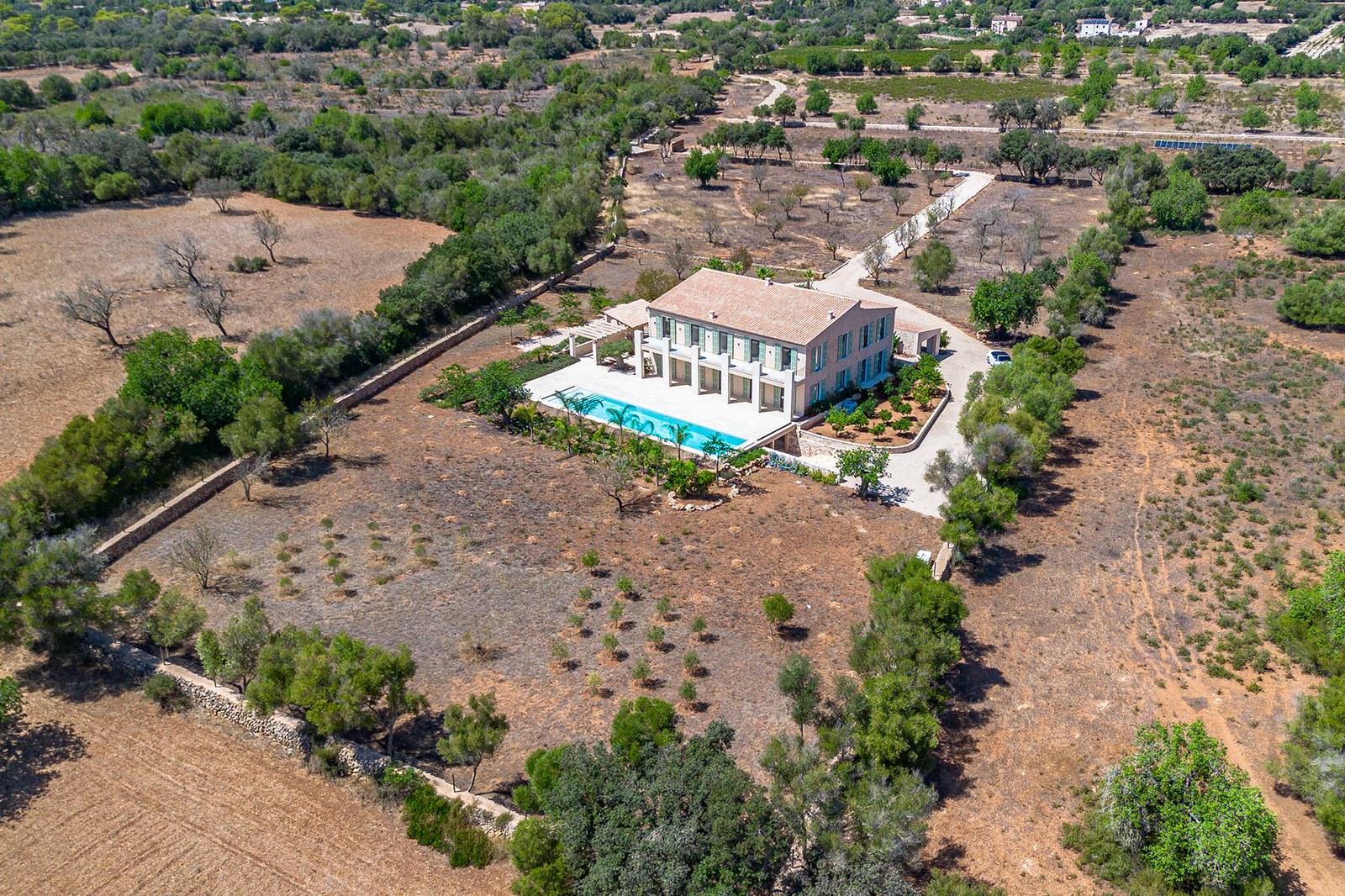 Vista aérea de una gran villa de dos plantas con piscina alargada, situada en una extensa finca rural con árboles.