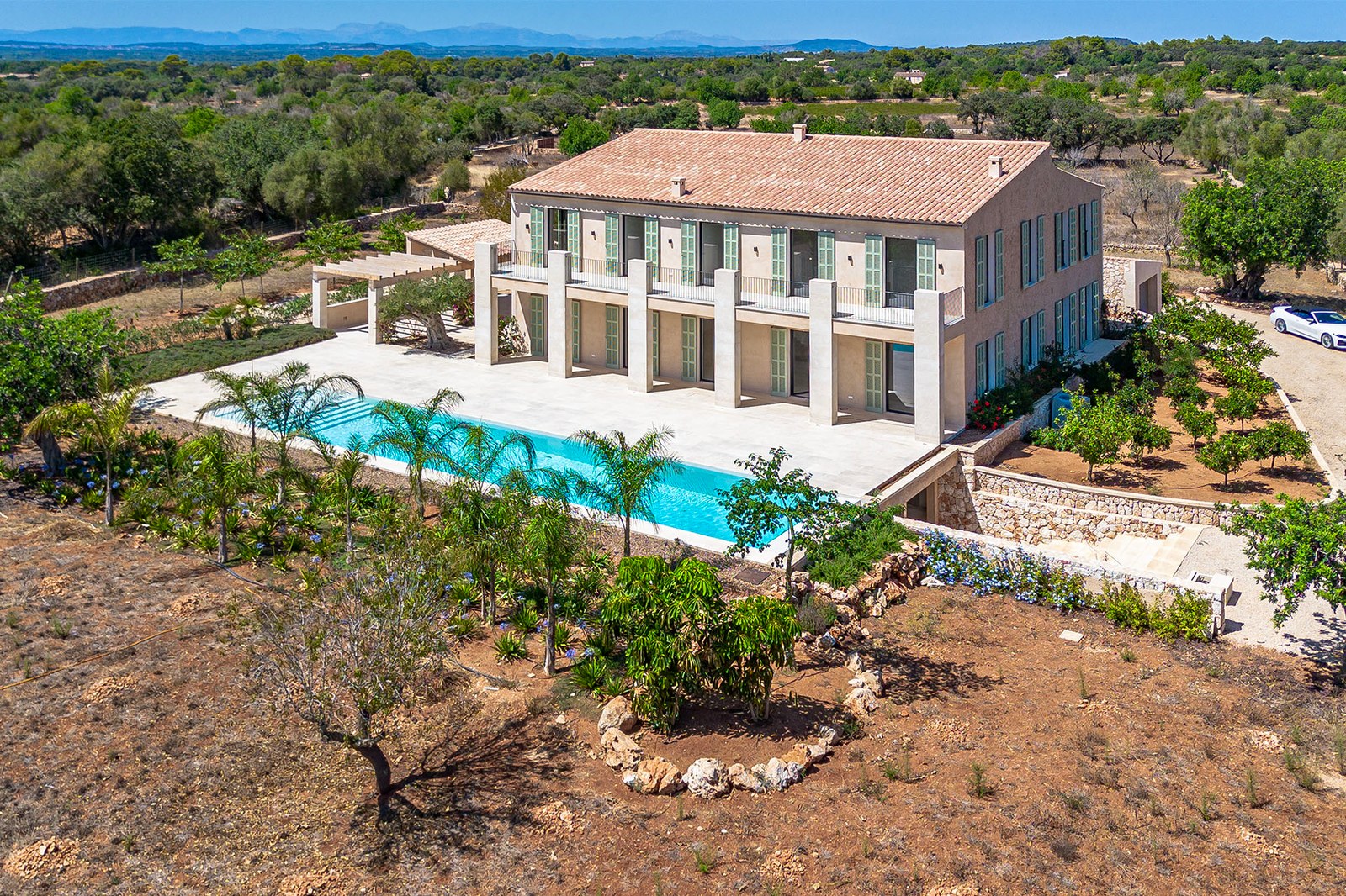 Vista aérea de una gran villa de piedra de dos plantas con piscina alargada y jardines en un entorno rural.