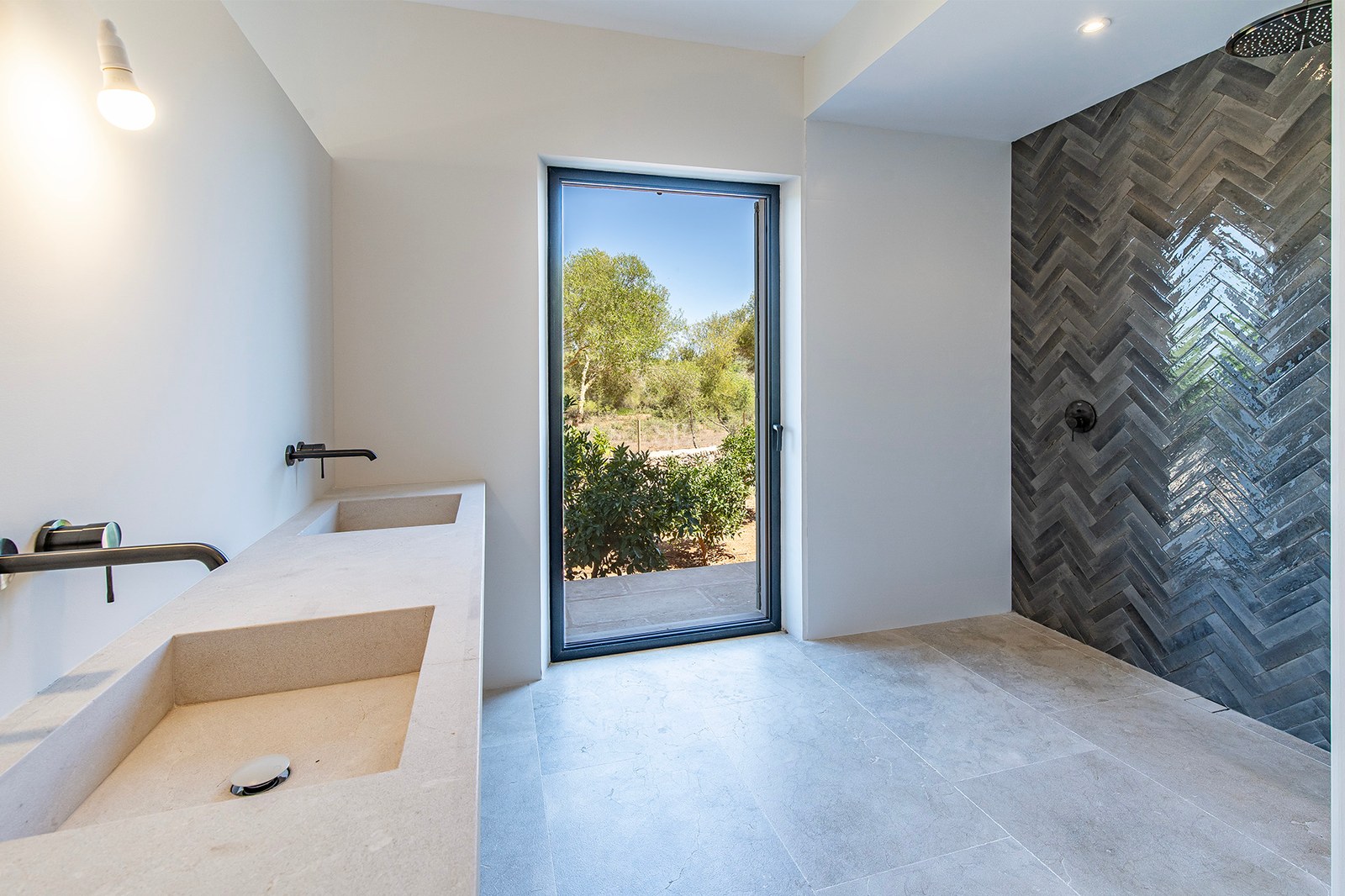 Baño de lujo con lavabo doble de piedra, grifería negra mate y ducha de azulejos en espiga con vistas al jardín.