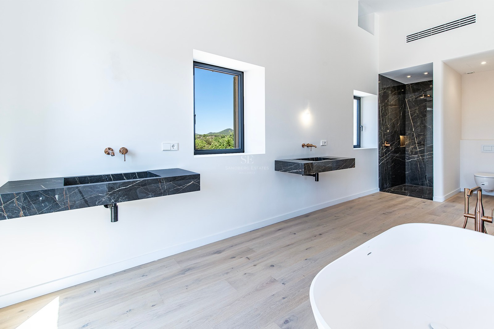 Baño principal luminoso con lavabos flotantes de mármol negro, suelos de roble y ducha de mármol.