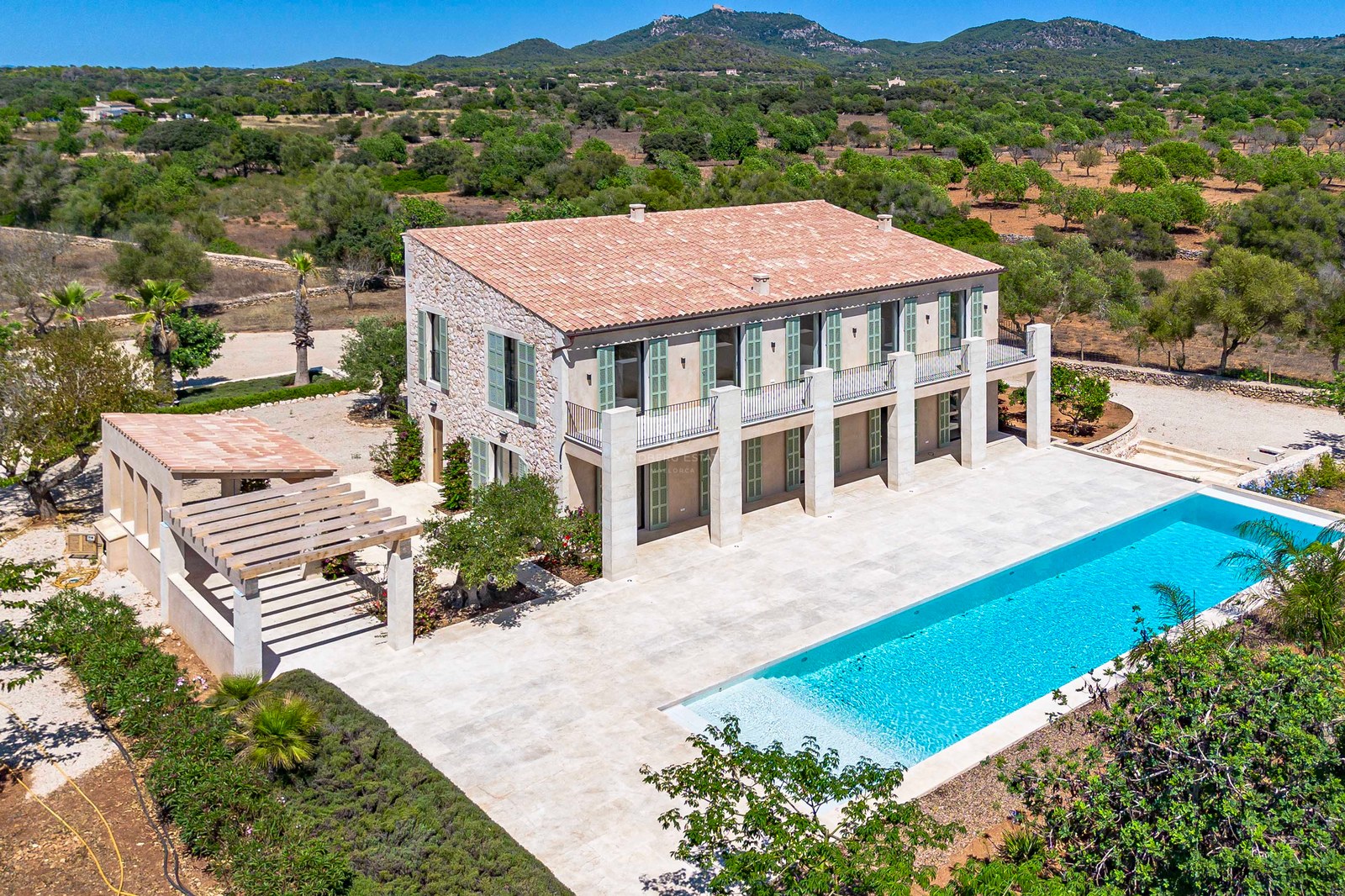 Vista aérea de una villa de piedra con piscina rectangular, persianas verdes y terraza de piedra natural.