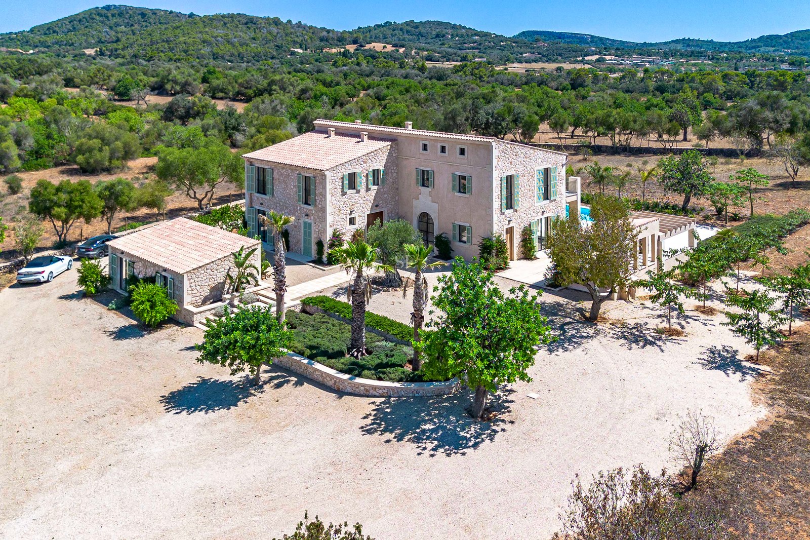 Vista aérea de una gran villa de piedra de dos plantas con casa de invitados, rodeada de paisaje mediterráneo.