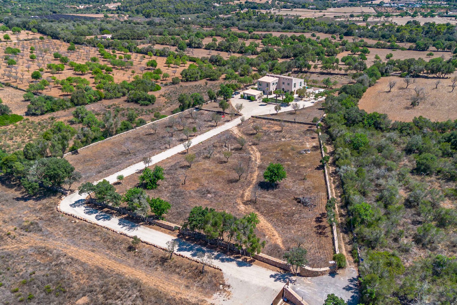 Vista aérea de una gran finca de piedra en una amplia parcela rodeada de muros de piedra seca y vegetación mediterránea.
