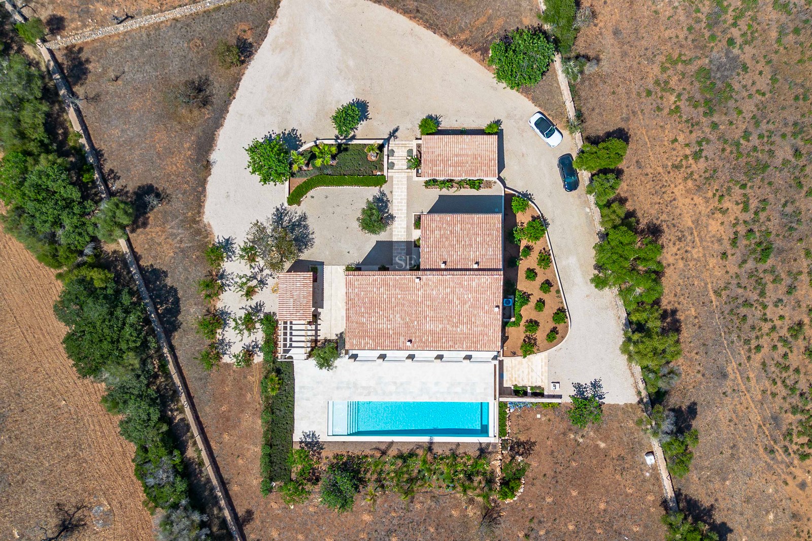 Vista cenital de una villa mediterránea con piscina, tejados de terracota y terrenos privados en el campo.