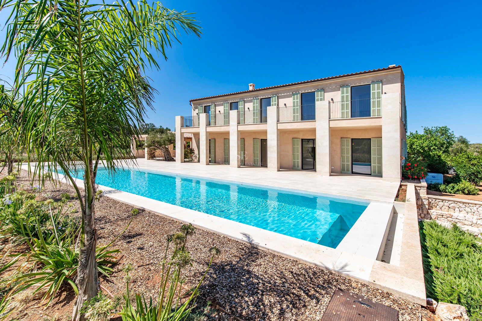 Villa moderna de dos plantas con fachada de piedra natural, persianas verdes y una piscina alargada turquesa.