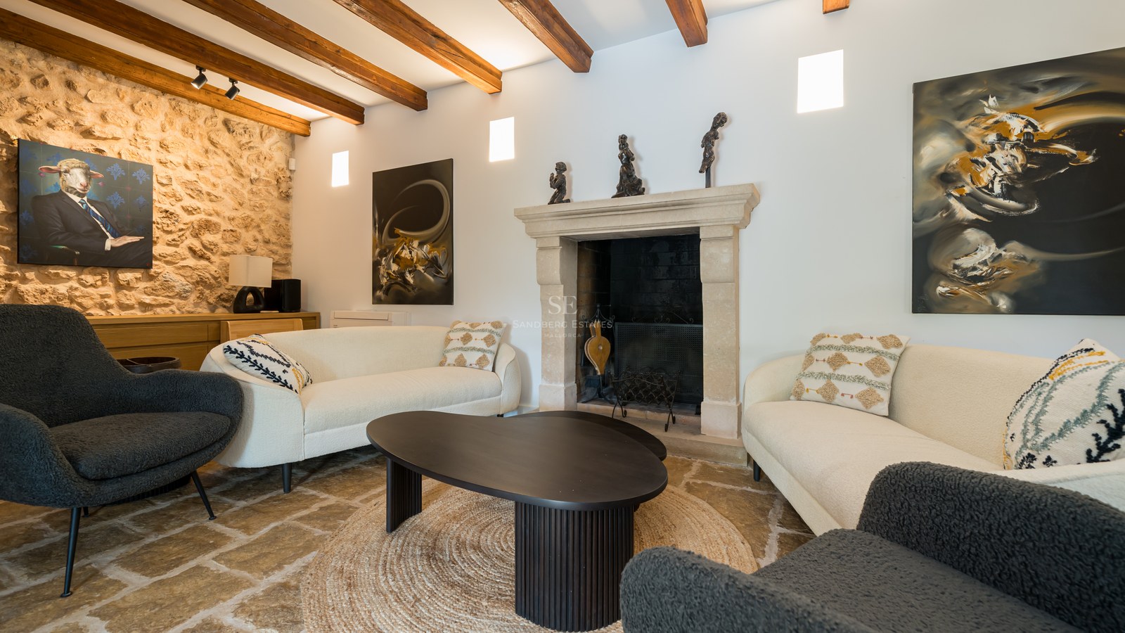 Modern living room with white sofas, stone fireplace, exposed wooden beams, and natural stone flooring.