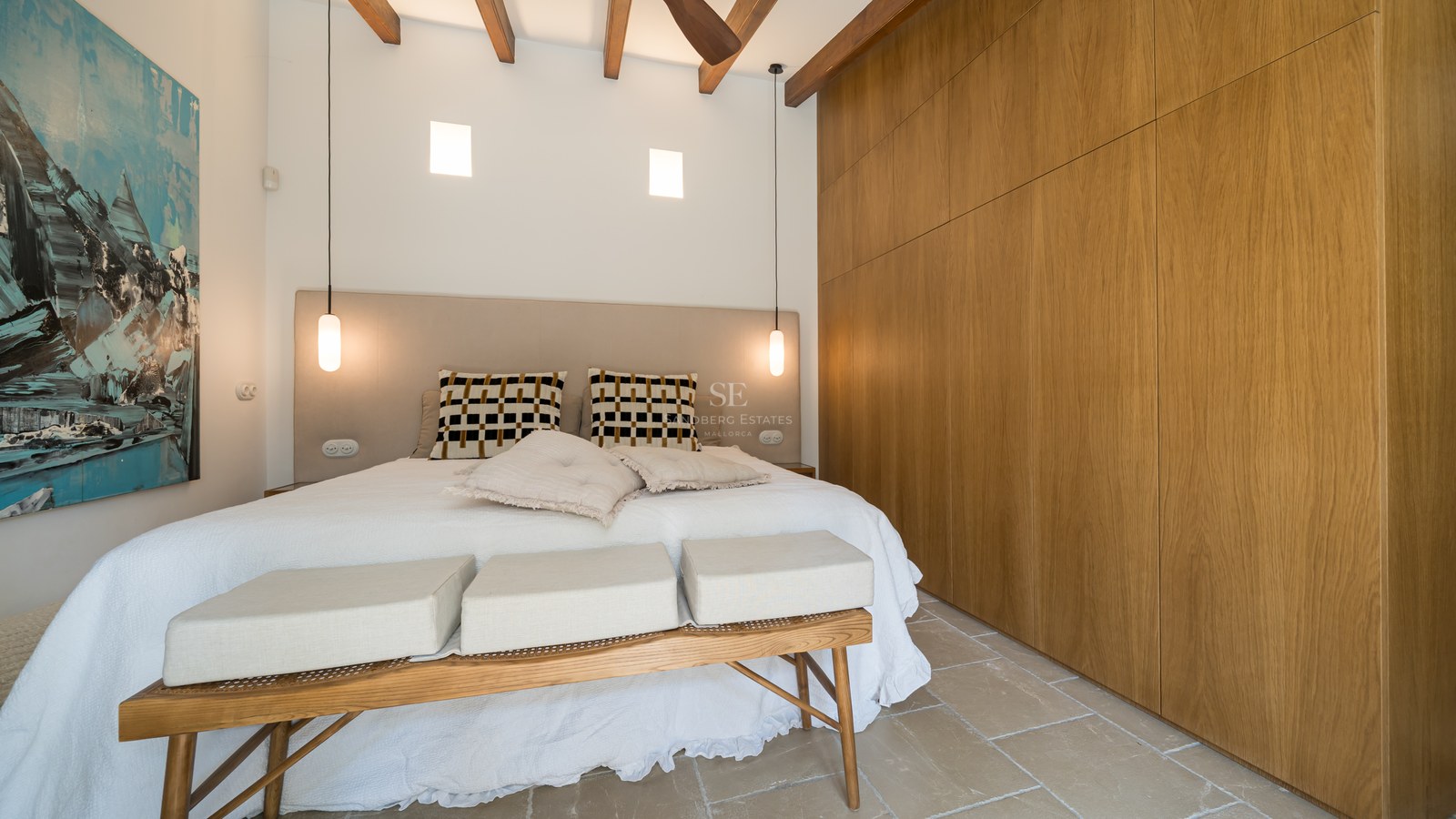 Modern bedroom featuring wood beam ceilings, large oak wardrobes, stone floors, and a blue abstract painting.