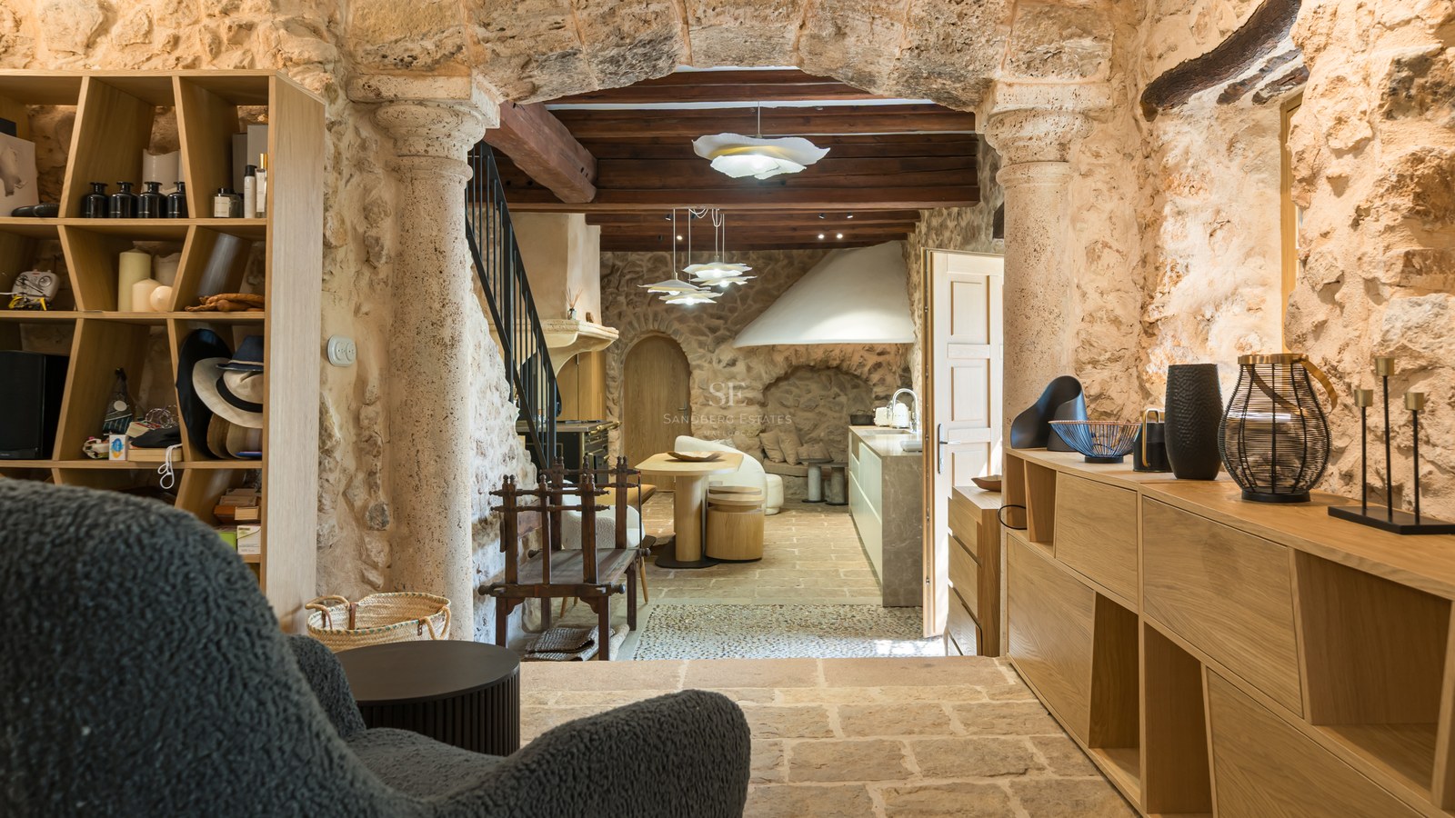 Interior view through a natural stone archway of a rustic kitchen with exposed wood beams and contemporary cabinetry.