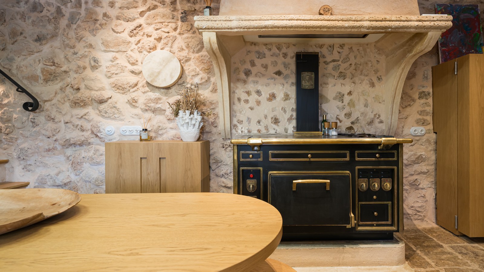 Bespoke black and brass Molteni stove set against a rustic natural stone wall in a luxury Mediterranean kitchen.