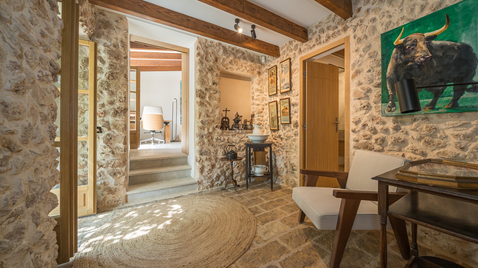 Entrance hallway featuring exposed natural stone walls, original timber ceiling beams, stone flooring, and a jute rug.