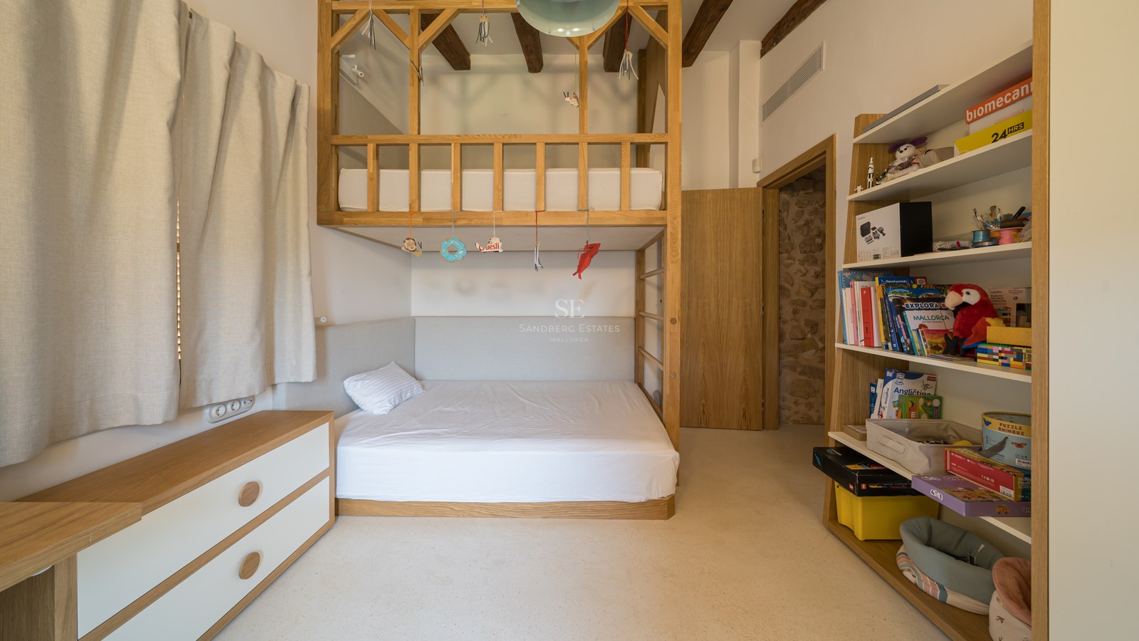 A light-filled children's bedroom featuring custom oak bunk beds, exposed ceiling beams, and integrated shelving.