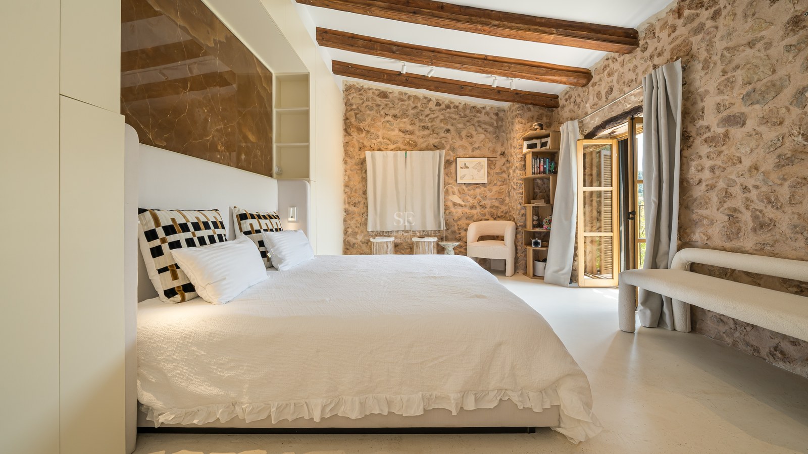 Spacious master bedroom featuring exposed natural stone walls, wooden ceiling beams, and a marble headboard panel.
