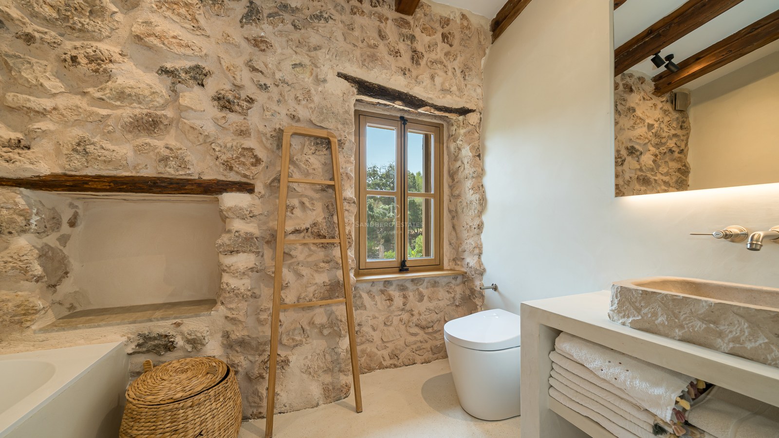 A luxurious bathroom featuring exposed natural stone walls, a hand-carved stone sink, and rustic wooden beams.