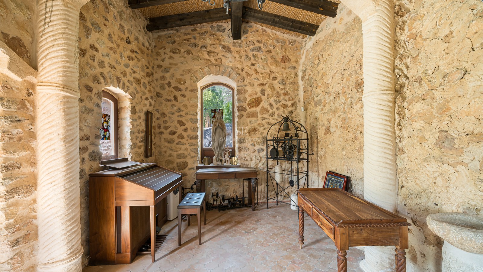 Interior of a traditional stone chapel featuring a wooden organ, religious statue, and vaulted timber ceiling.