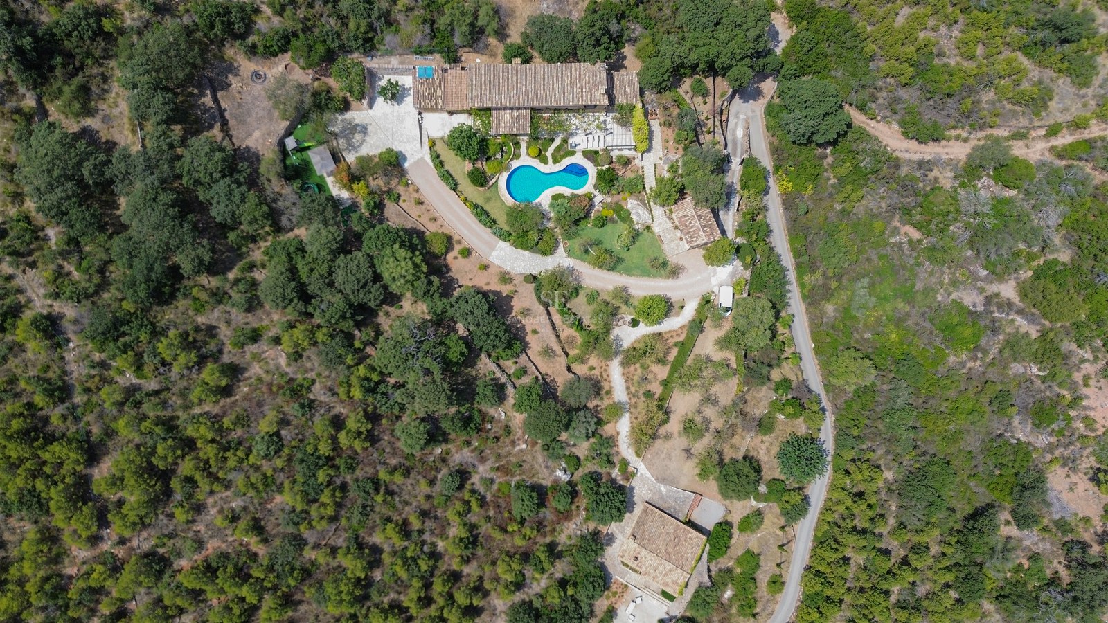 Vista aérea de una villa con tejados de terracota, piscina azul y jardines rodeados de bosque denso.