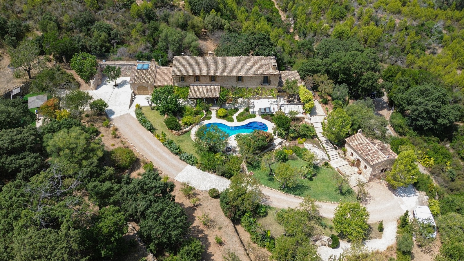 Vista aérea de una villa de piedra con piscina privada rodeada de frondoso bosque mediterráneo.