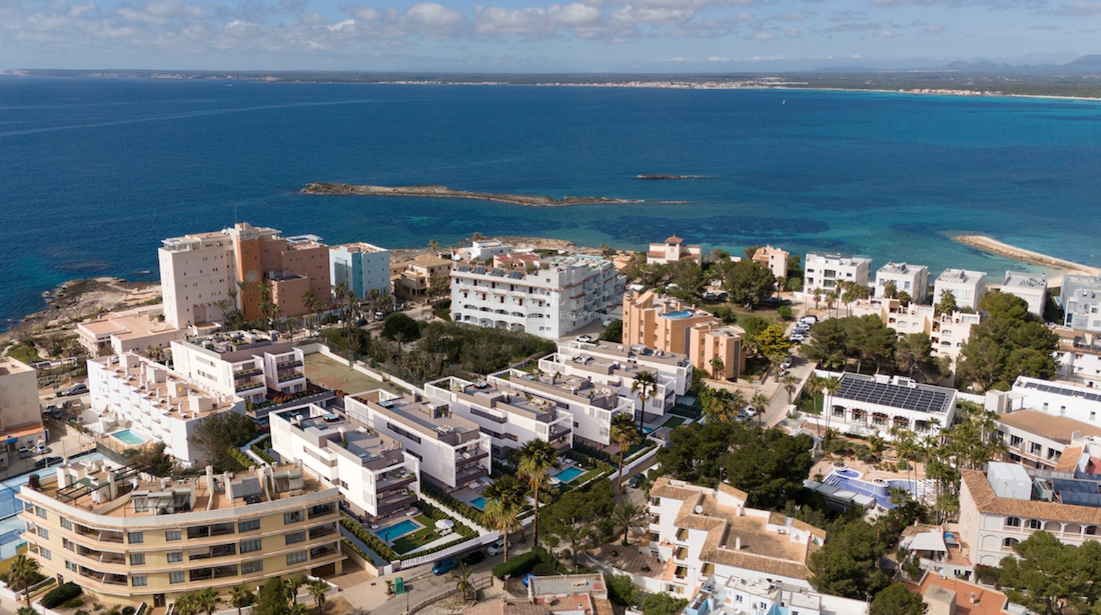 Aerial drone view of white modern apartment complexes and private pools overlooking a deep blue Mediterranean sea.