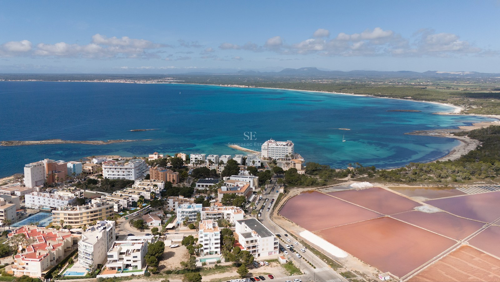Drone view of turquoise Mediterranean sea, white seaside architecture, and vibrant pink salt evaporation ponds.