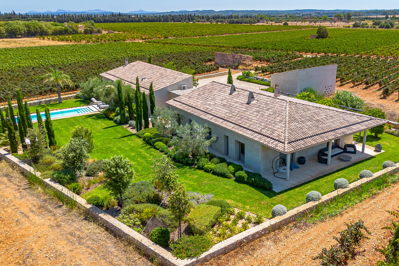 Vue aérienne d'une villa contemporaine avec toits de tuiles, piscine et jardins au milieu de vastes vignobles.