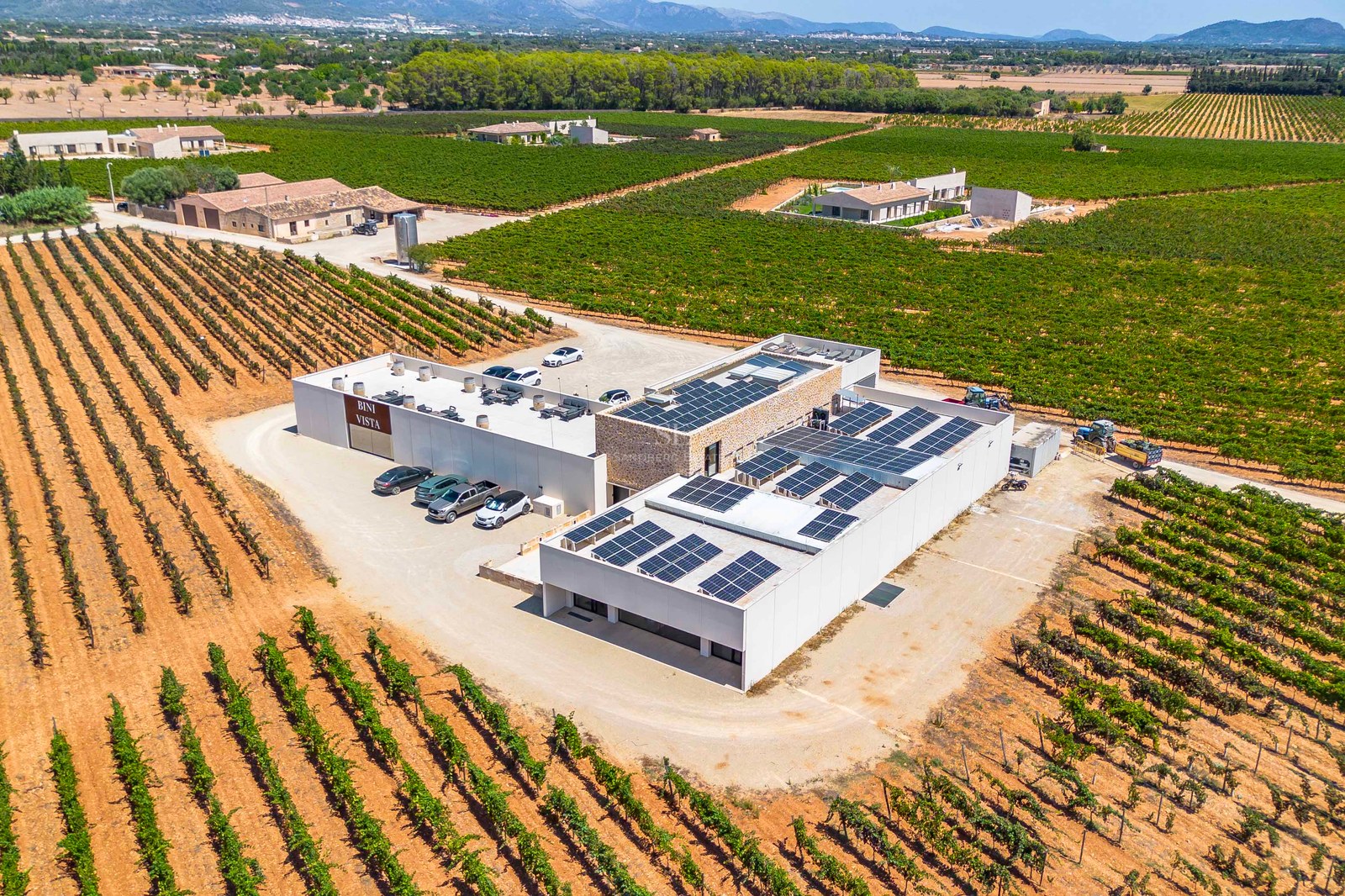 Vue aérienne d'un domaine viticole contemporain entouré de vastes vignobles et de montagnes en arrière-plan.