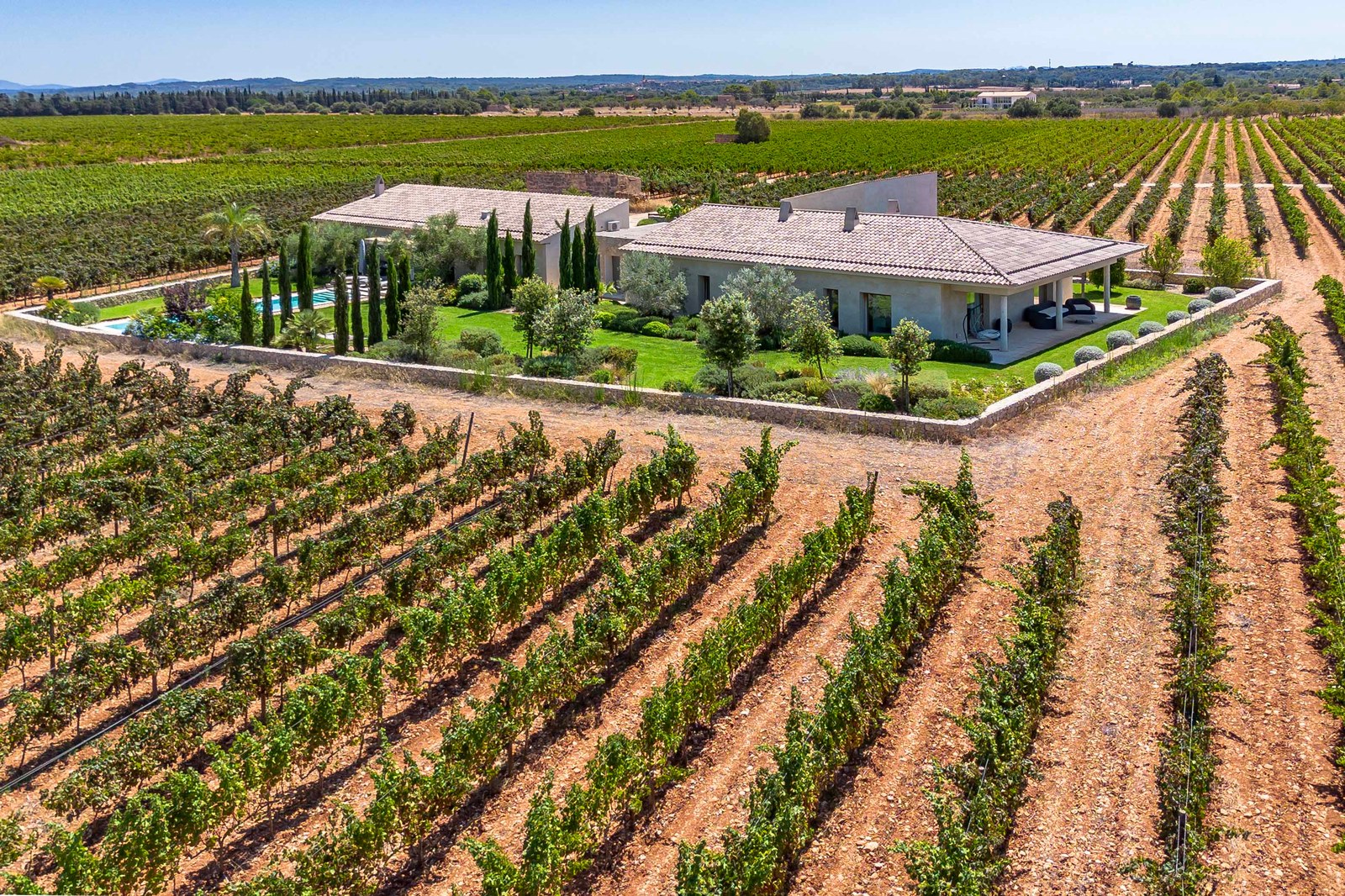 Vue aérienne d'une villa moderne en pierre nichée au centre de vastes vignobles verdoyants et de jardins soignés.
