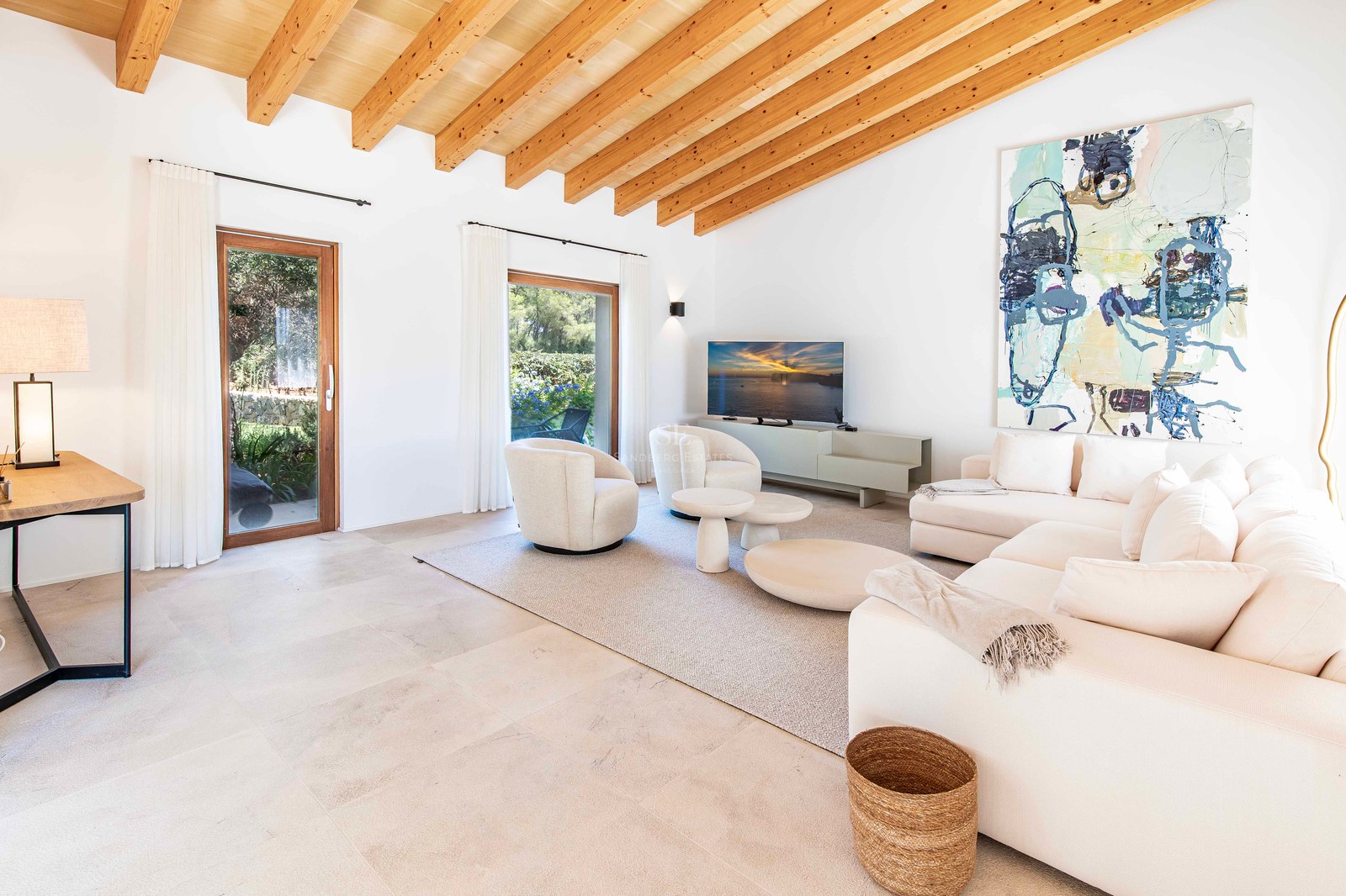 Salon moderne avec haut plafond à poutres, canapés blancs, sol en pierre naturelle et accès au jardin.