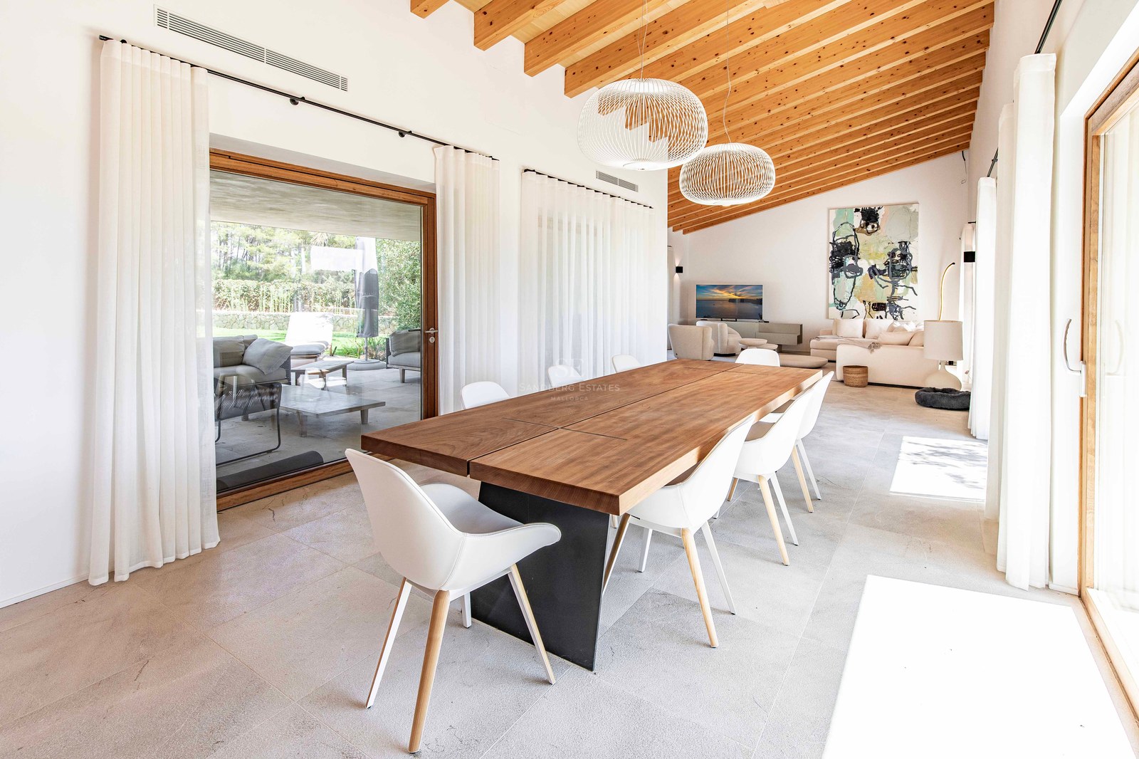 Salle à manger moderne avec table en bois, plafond voûté en bois et baies vitrées donnant sur la terrasse.