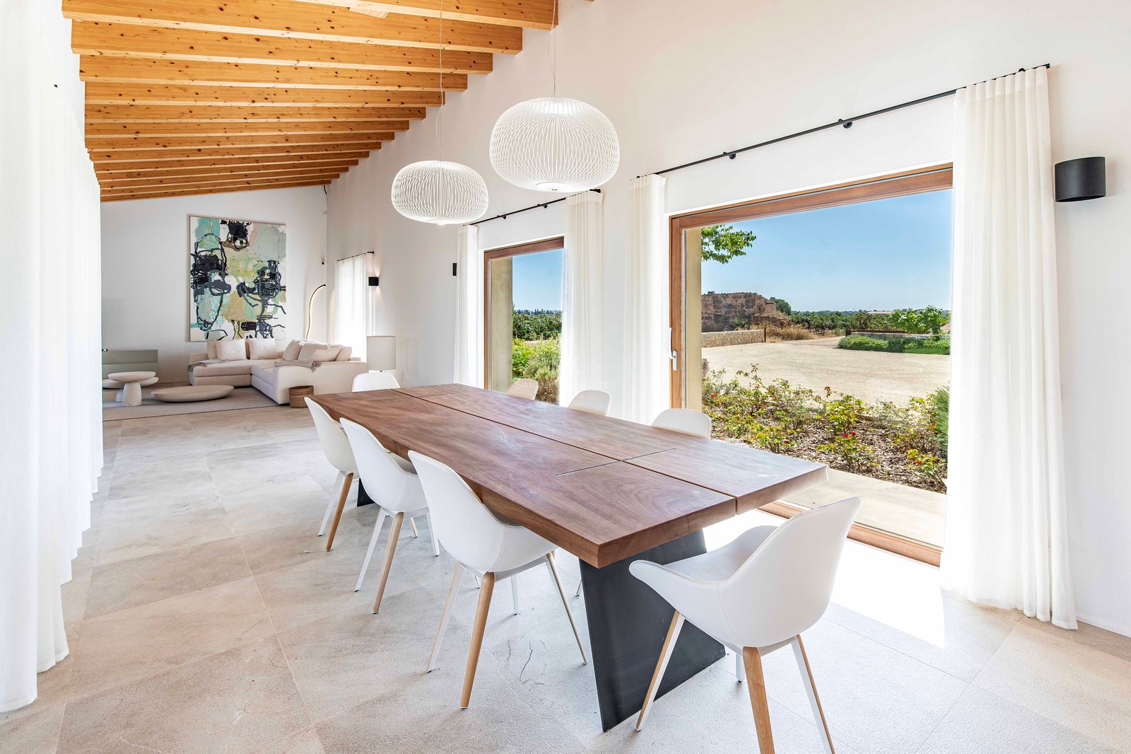 Intérieur d'une salle à manger lumineuse avec table en bois, chaises blanches et plafond à poutres.