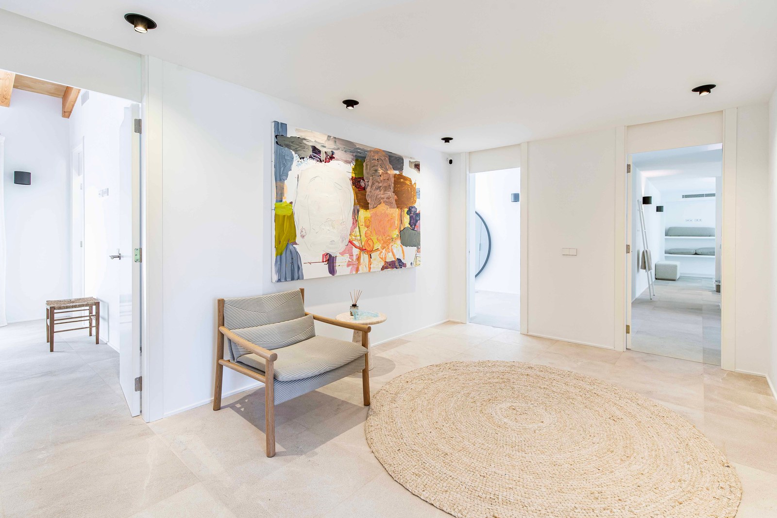 Couloir minimaliste avec sol en pierre naturelle, tapis rond en jute, fauteuil en bois et peinture abstraite.