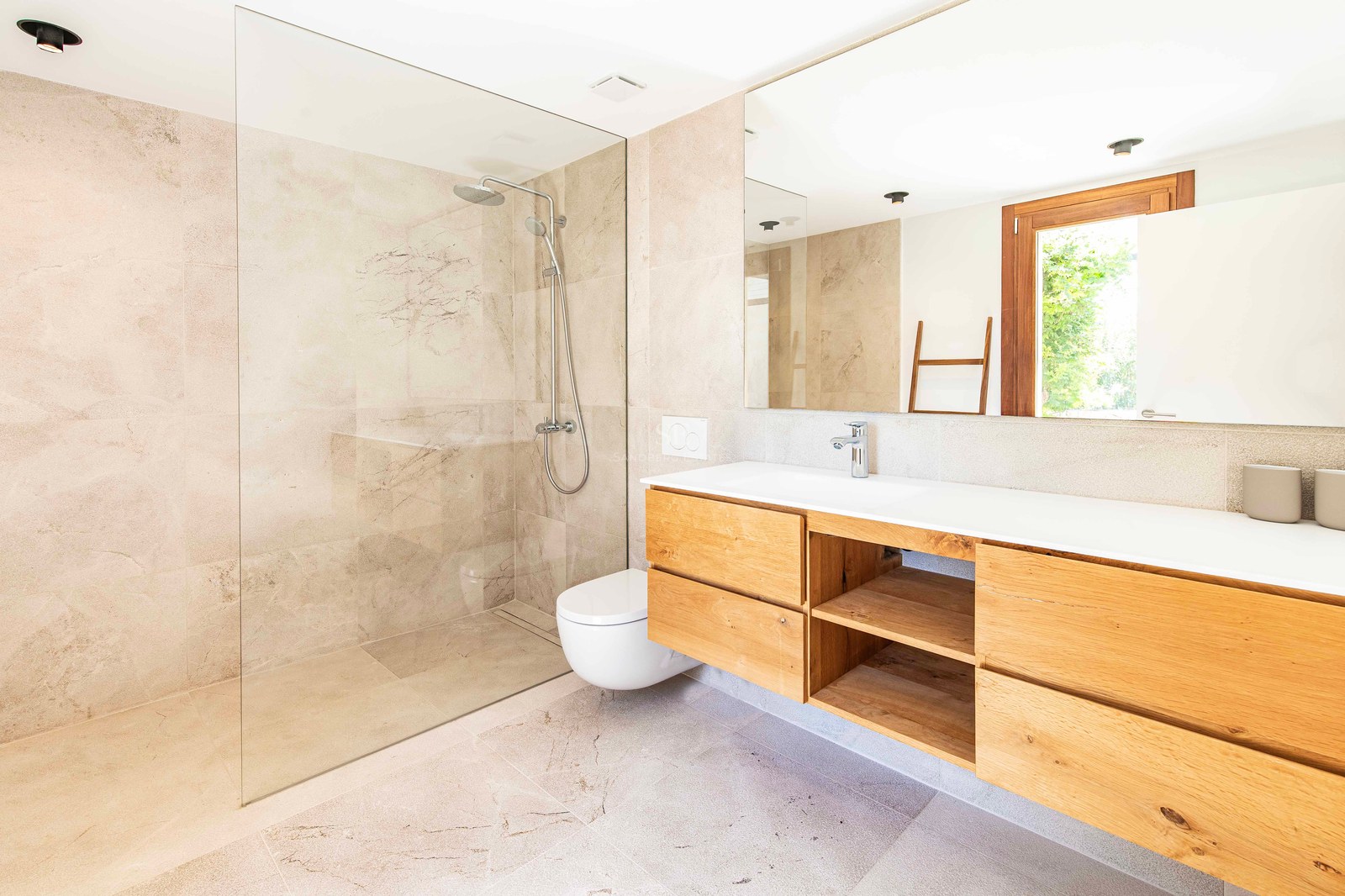 Salle de bain moderne avec douche à l'italienne, paroi en verre, meuble vasque en chêne et carrelage en pierre beige.