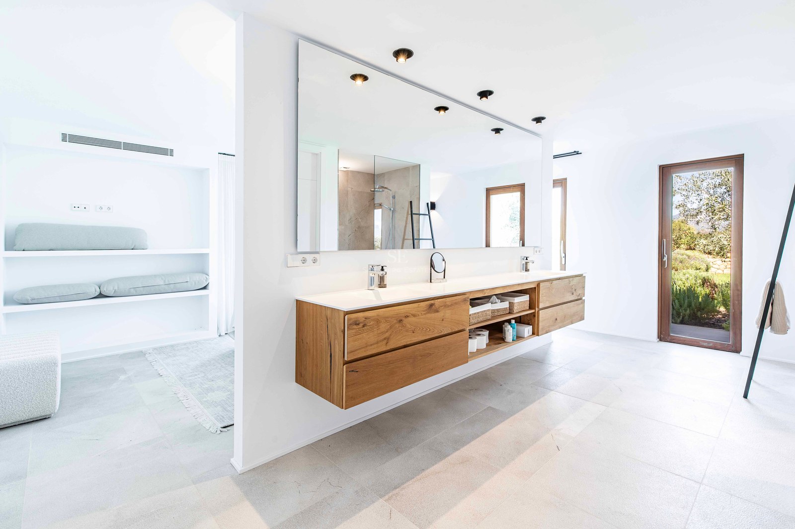 Salle de bains moderne avec double vasque suspendue en chêne, grand miroir et porte vitrée sur jardin.