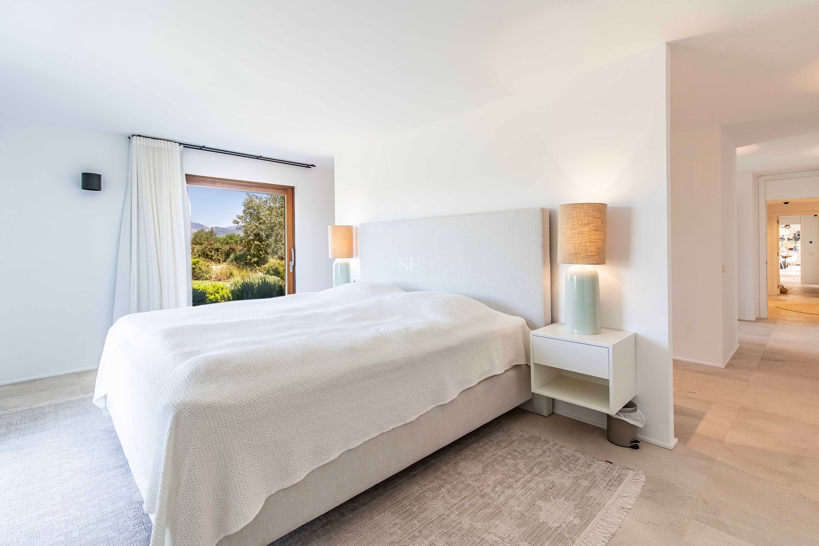 Chambre parentale lumineuse et moderne avec sol en pierre, lit rembourré et fenêtre donnant sur la verdure.