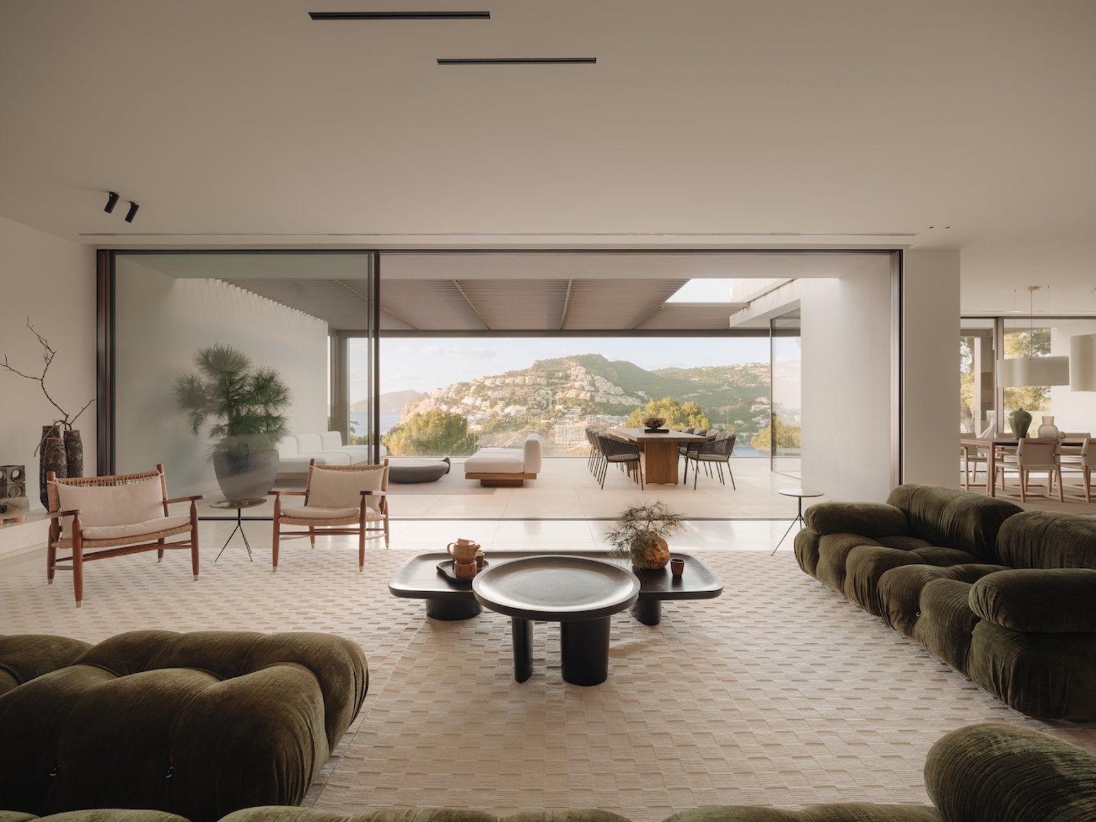 Salón de lujo con sofás de terciopelo verde y ventanales de suelo a techo que abren a una terraza con vistas.