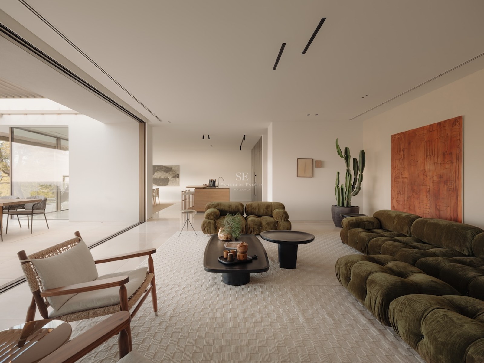 Salón moderno con sofás de terciopelo verde oliva y grandes ventanales que dan a una terraza luminosa.