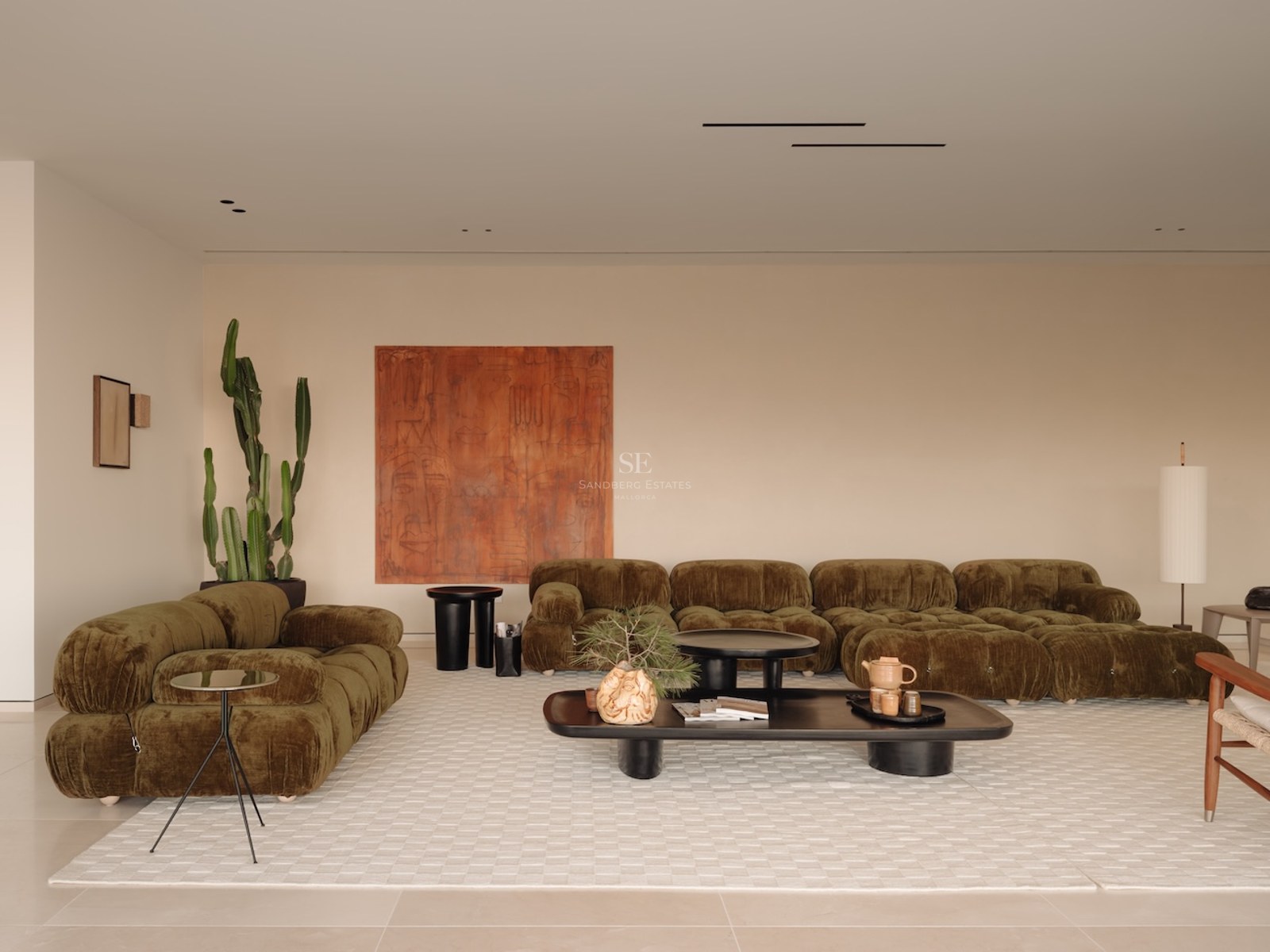 Salón moderno con sofás modulares verde oliva, un cuadro abstracto grande y una alfombra blanca con textura.