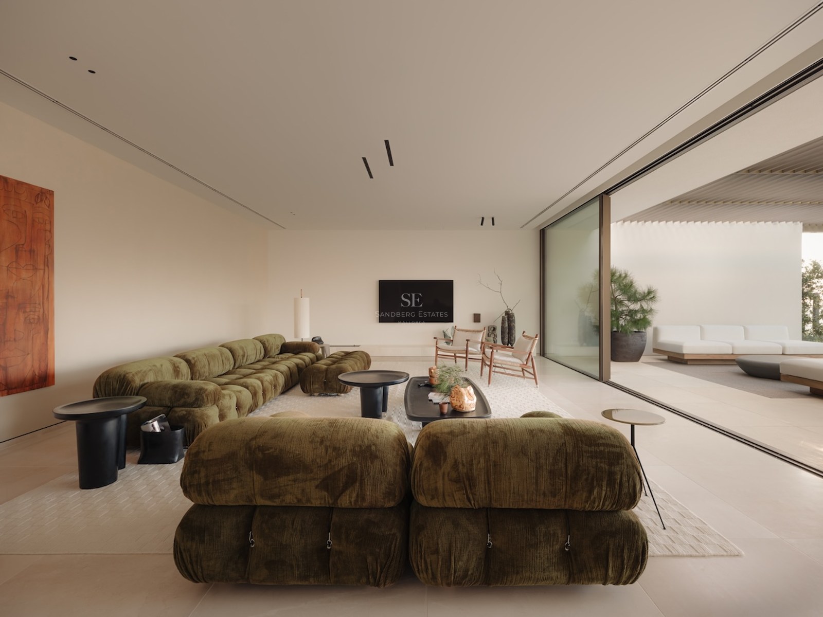 Salón moderno con sofá modular verde oliva y grandes ventanales que conectan con una terraza soleada.