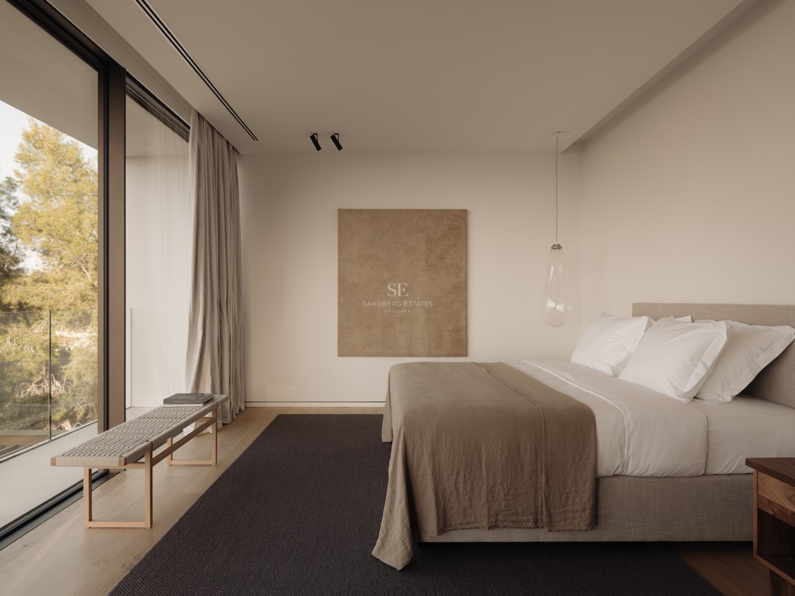 Dormitorio minimalista con ventanales de suelo a techo, suelo de madera, ropa de cama de lino y vistas a los árboles.