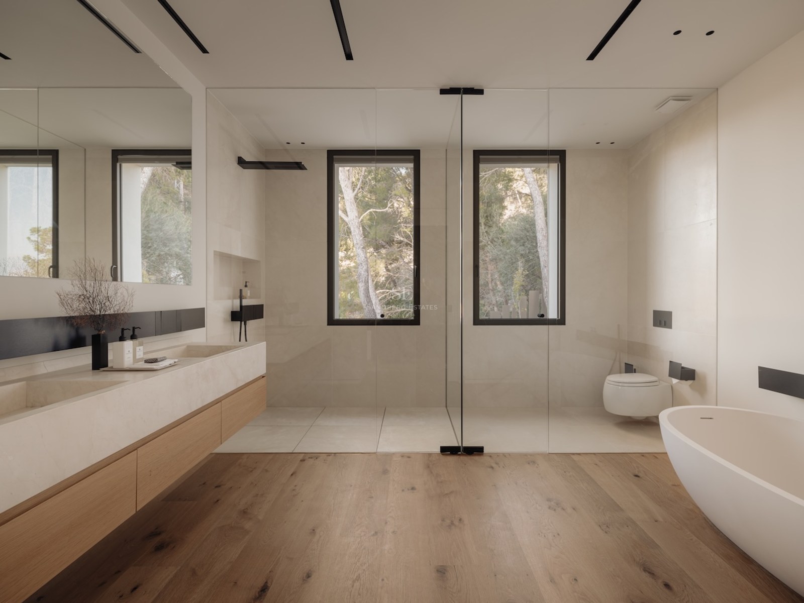 Baño moderno con suelos de roble, lavabo doble de piedra, bañera exenta y ducha frente a ventanales con pinos.