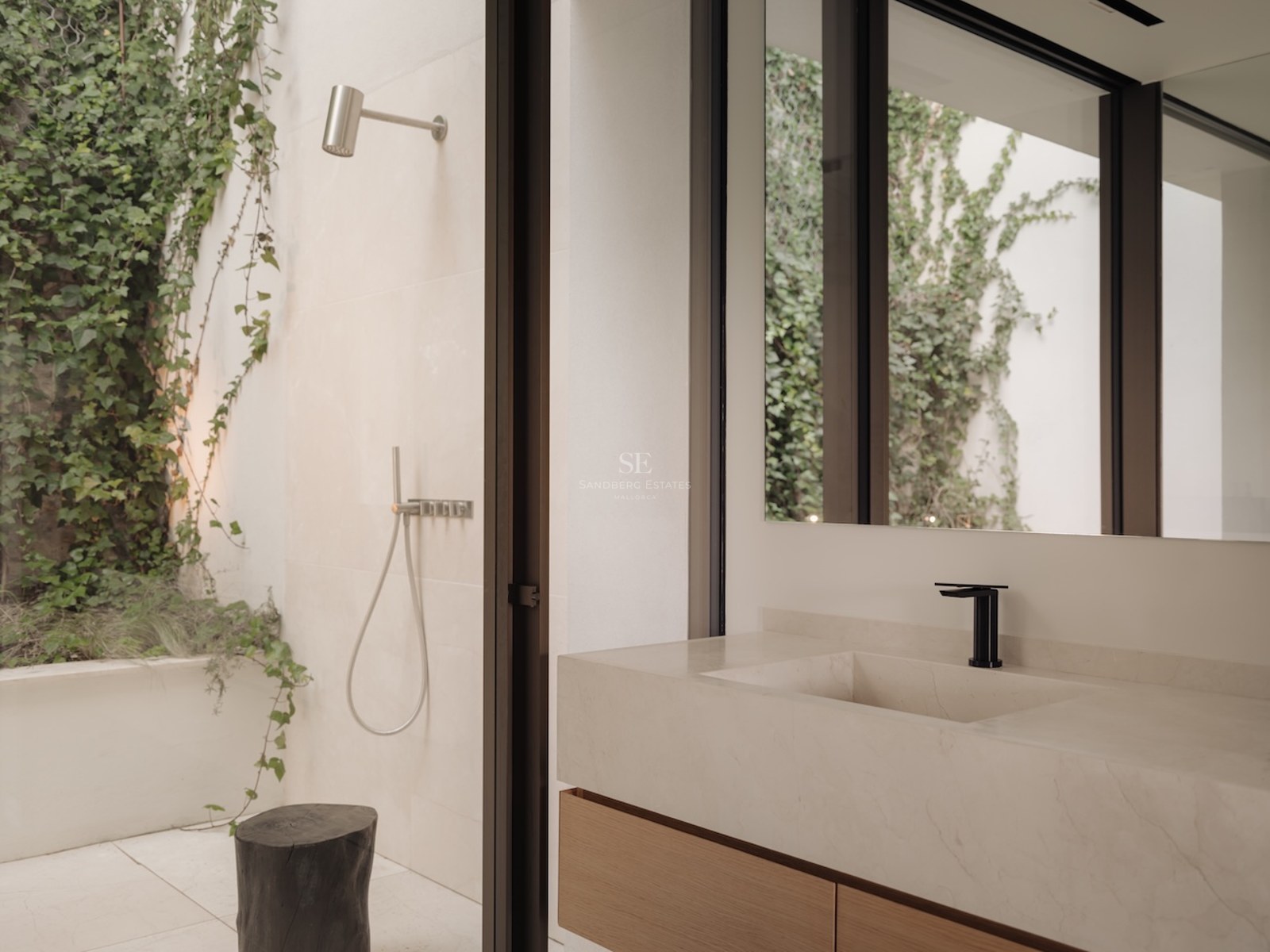 Tocador de baño minimalista con lavabo de piedra y vista a ducha exterior en patio con pared de hiedra verde.