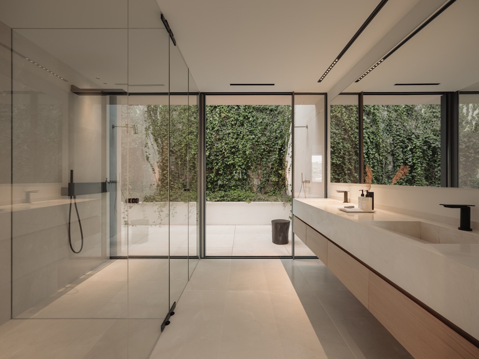 Baño moderno con amplia ducha de cristal, lavabo de piedra y vistas a un patio privado con muro verde.