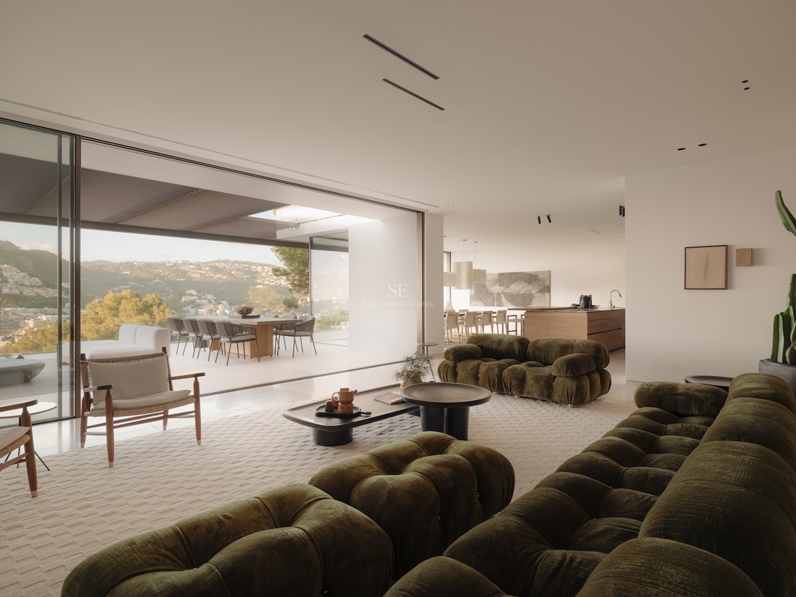 Salón contemporáneo con sofás verde oliva abierto a una terraza soleada con vistas a las colinas.