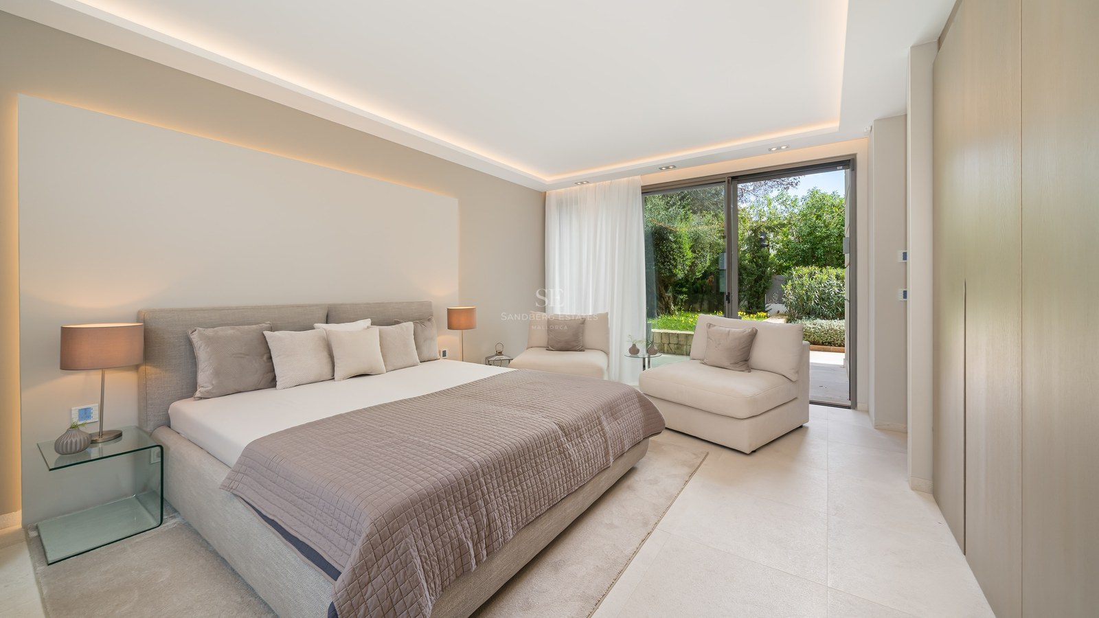 Contemporary bedroom with neutral tones, large bed, glass bedside table, and sliding doors opening to a lush garden.