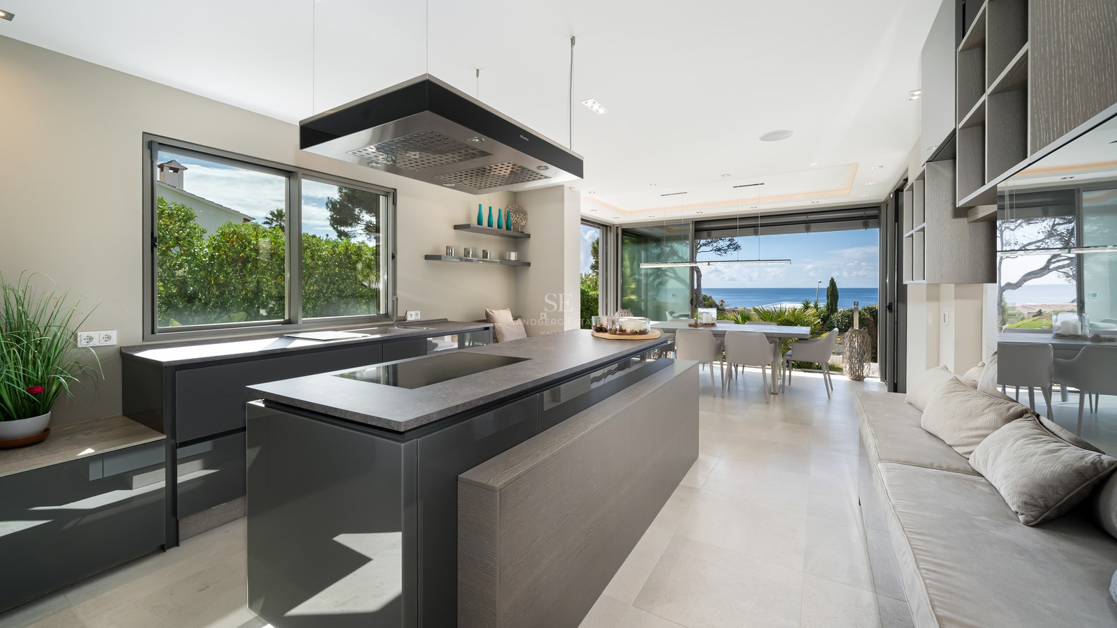 Modern kitchen featuring a charcoal grey island, designer extractor, and floor-to-ceiling windows with Mediterranean views.