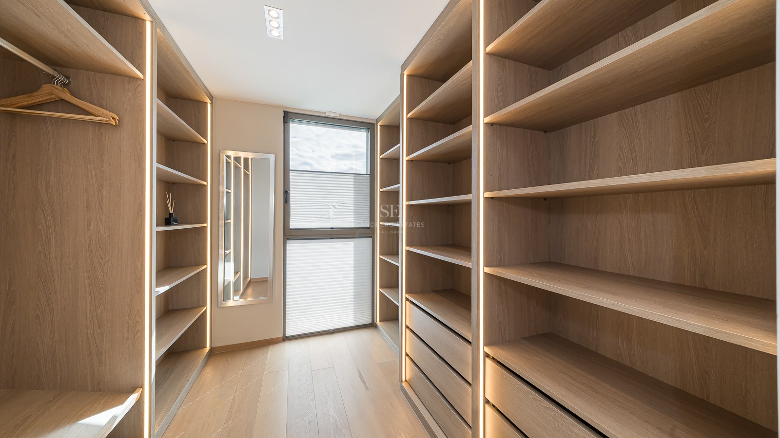 Custom oak-finished walk-in closet with integrated vertical LED lighting and a full-length mirror.