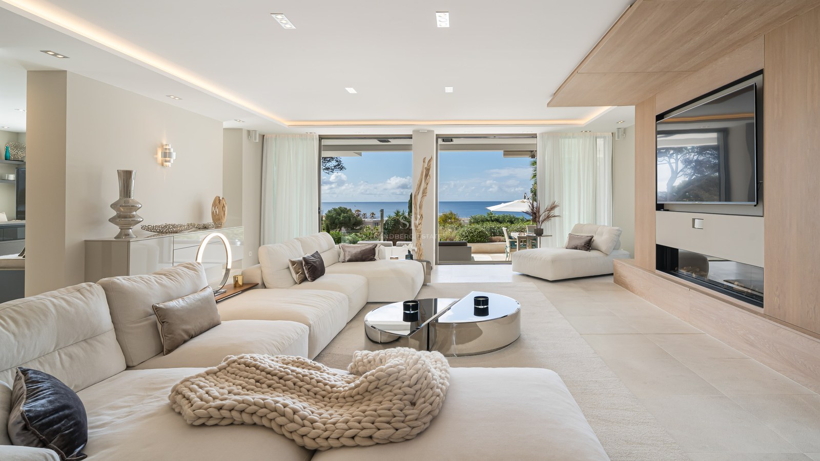 Modern living room with white sofas, oak wood accents, and large glass doors overlooking the Mediterranean Sea.