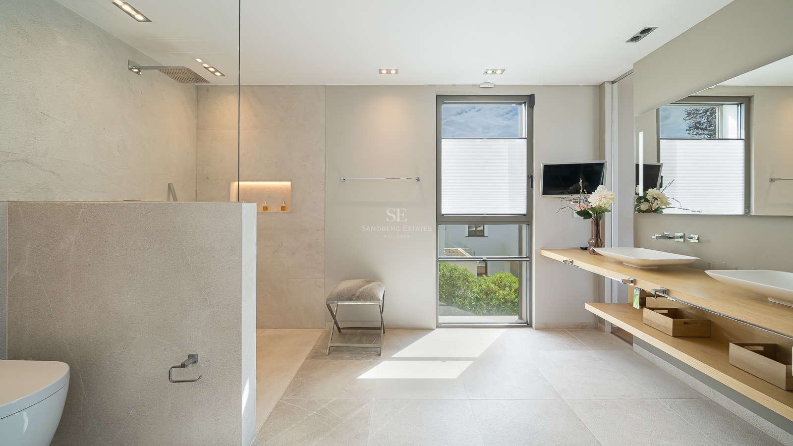 Contemporary bathroom featuring double wooden vanity, beige stone tiling, and glass-enclosed rain shower.